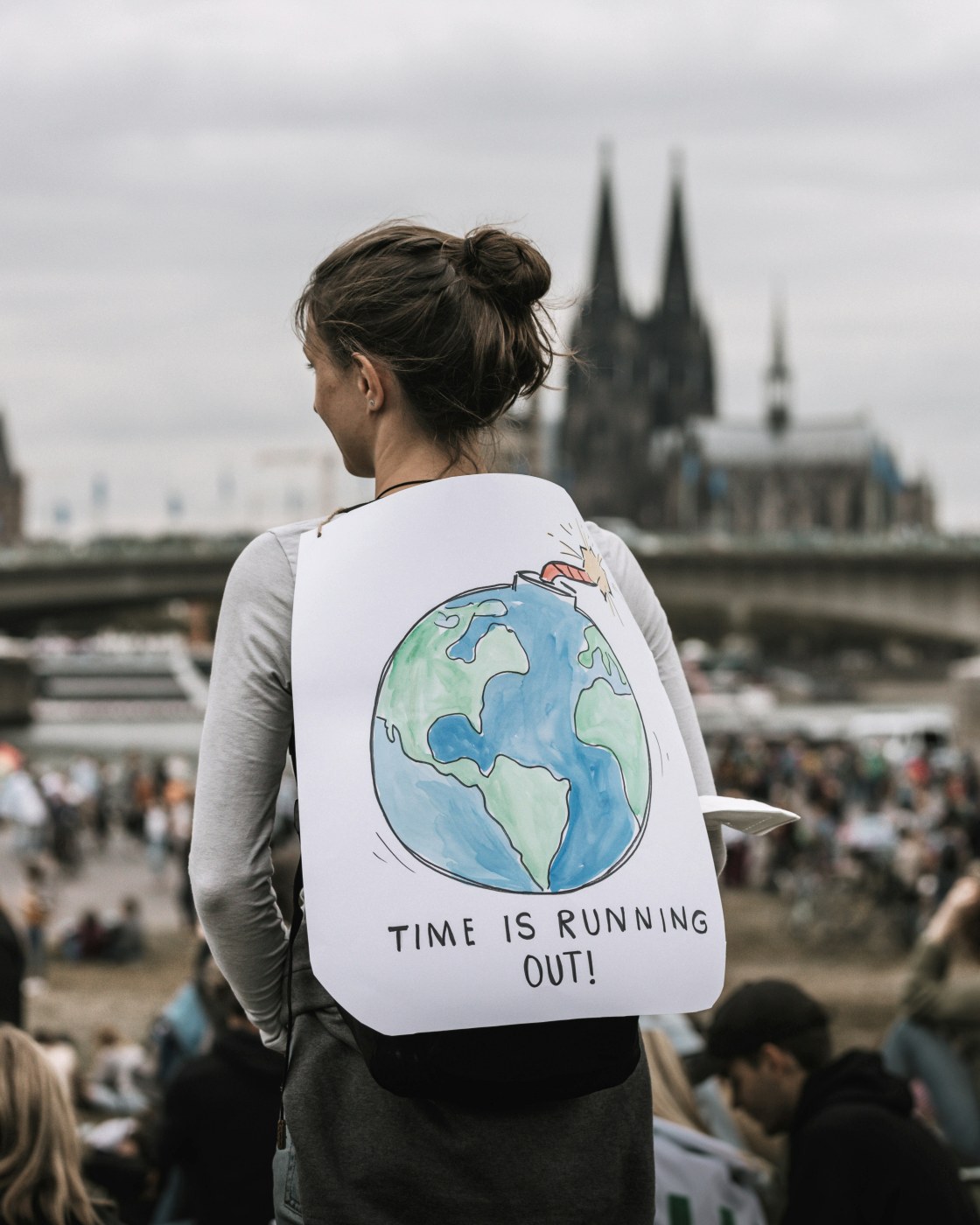 a person at a climate change protest, holding a sign saying time is running out with a picture of the earth looking with time ticking down